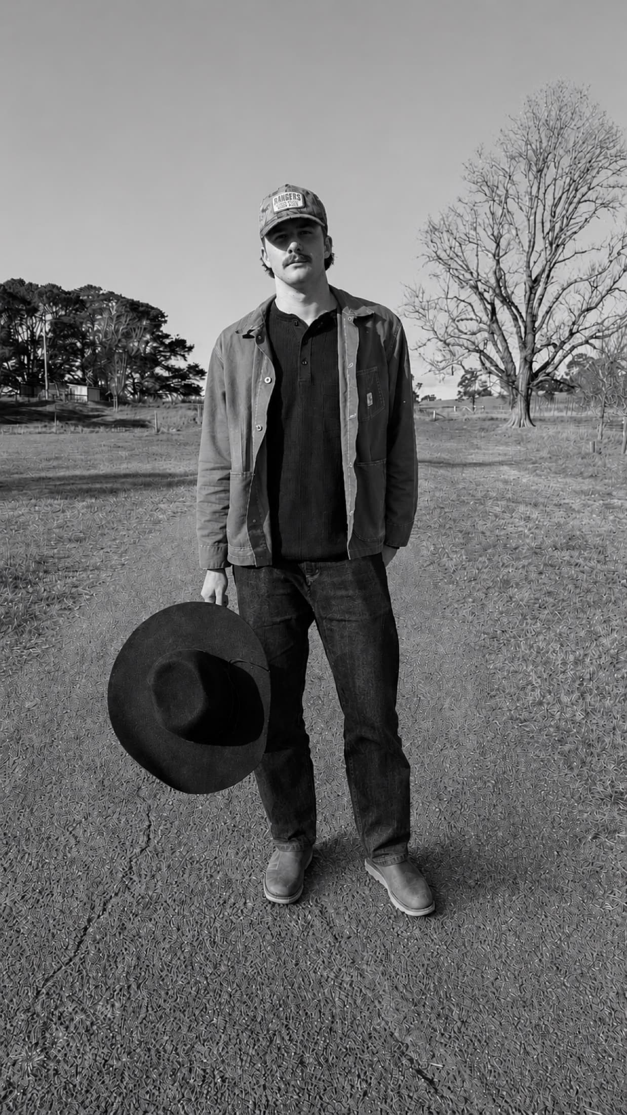 Kai Rennie holding his hat on a country road
